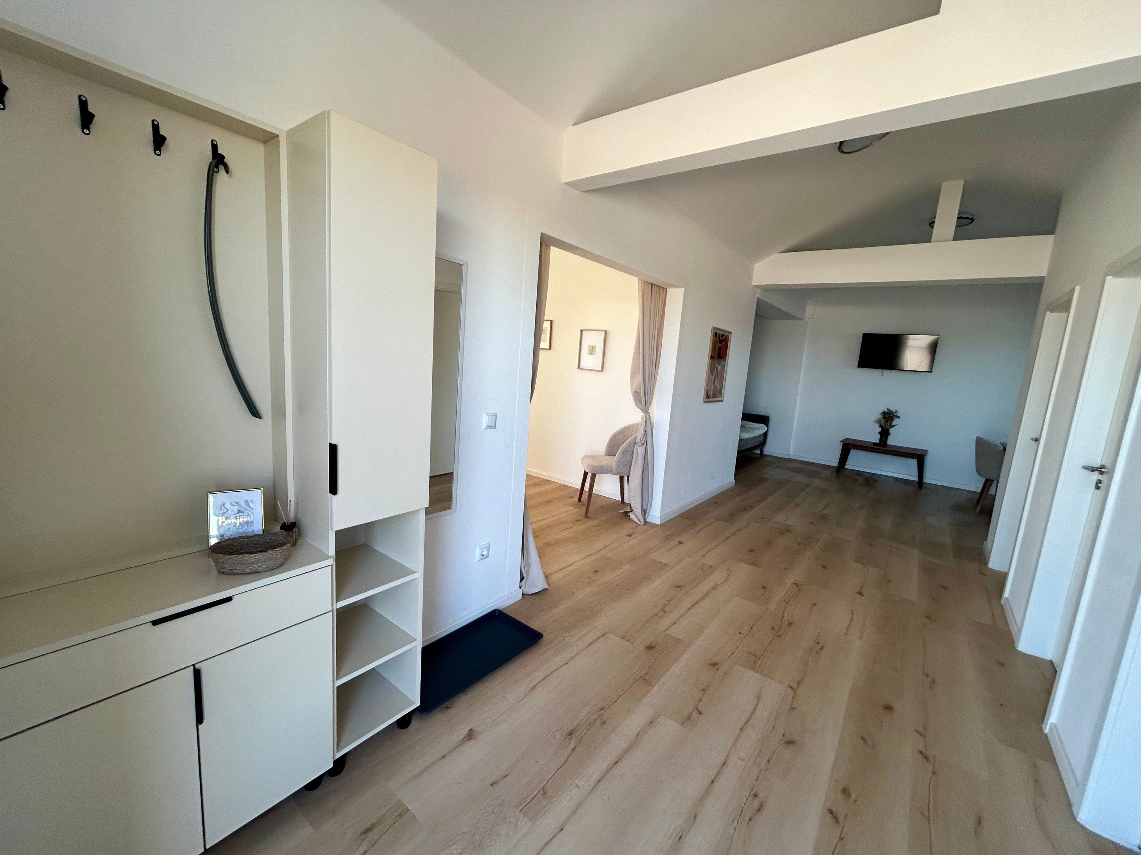 Una habitación amplia con piso de madera, un armario blanco, una mesita y una silla.
