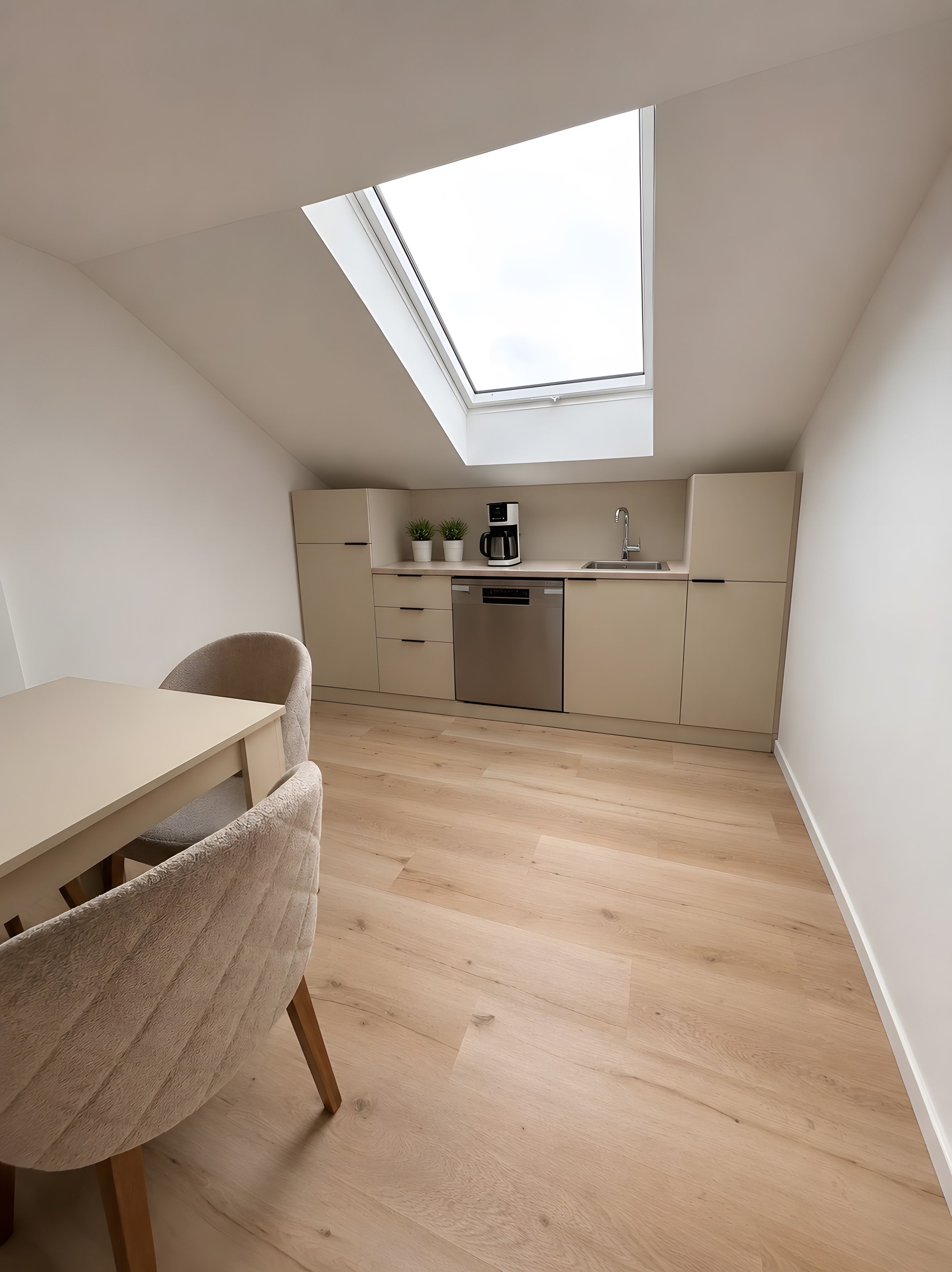 Une cuisine compacte dotée d’une lucarne, d’un plancher en bois et d’un coin repas avec une chaise.
