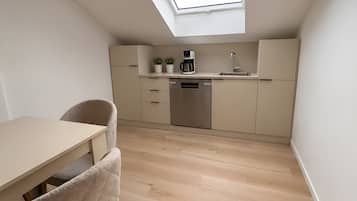 Une cuisine compacte dotée d’une lucarne, d’un plancher en bois et d’un coin repas avec une chaise.