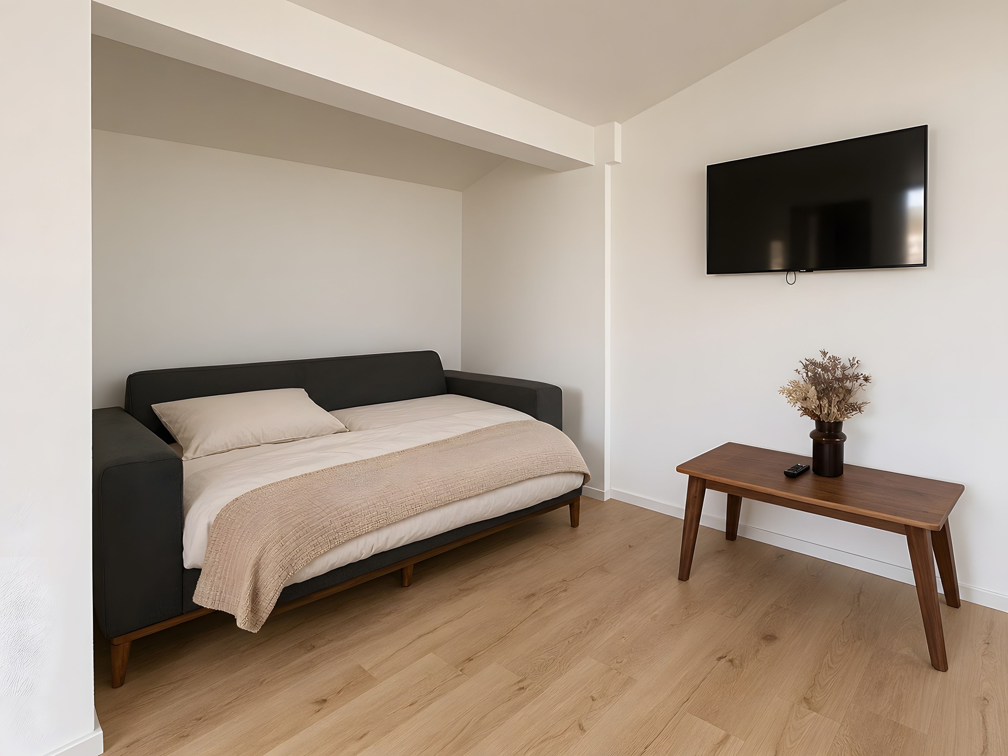 A bedroom with a bed, a TV mounted on the wall, and a small wooden table with a vase.
