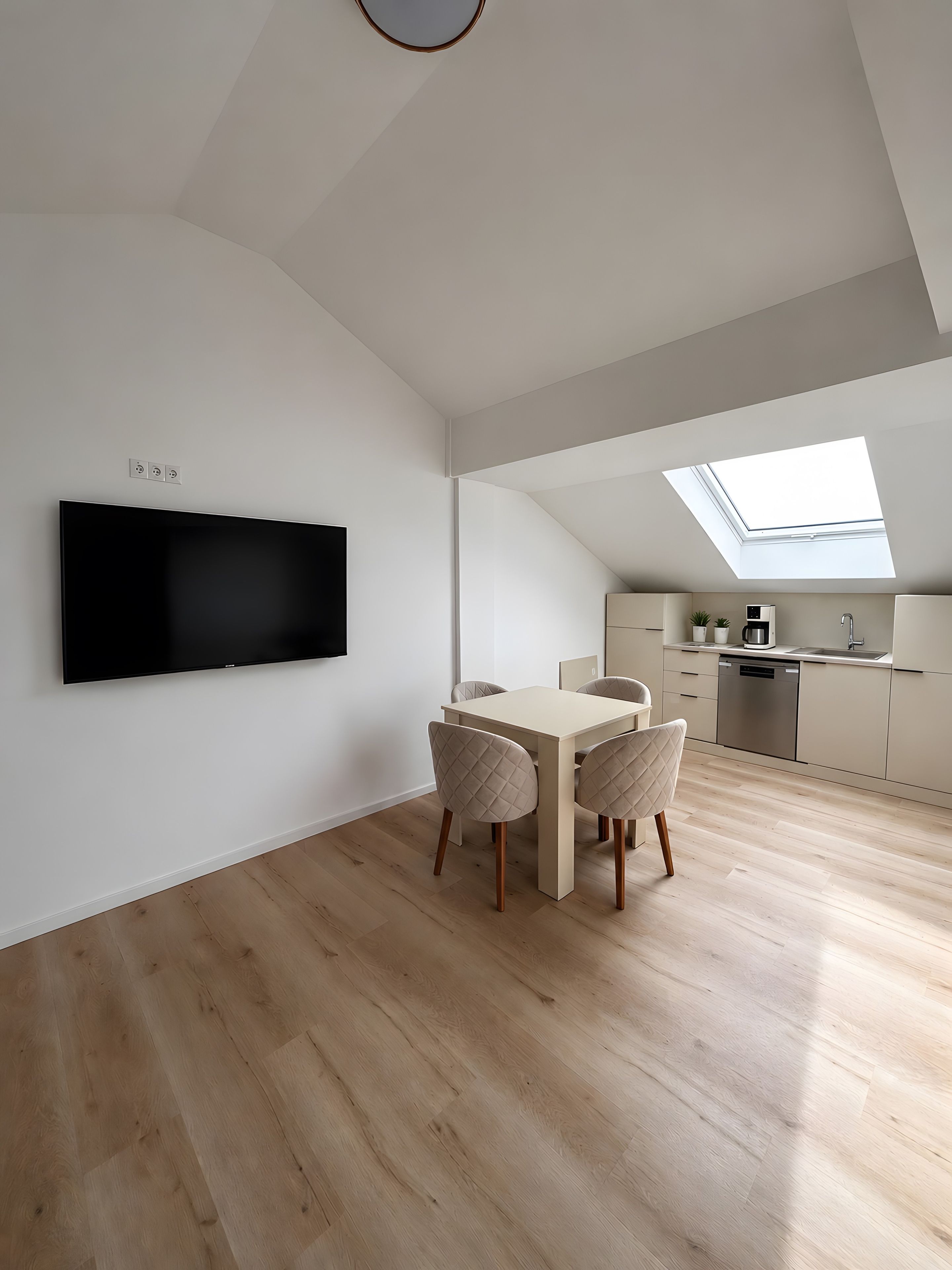 Un appartement moderne de style «loft» comprenant un coin repas, une cuisine et un grand téléviseur fixé au mur.
