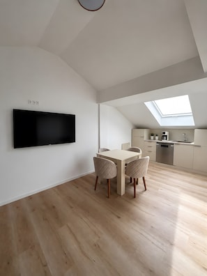 Un appartement moderne de style «loft» comprenant un coin repas, une cuisine et un grand téléviseur fixé au mur.