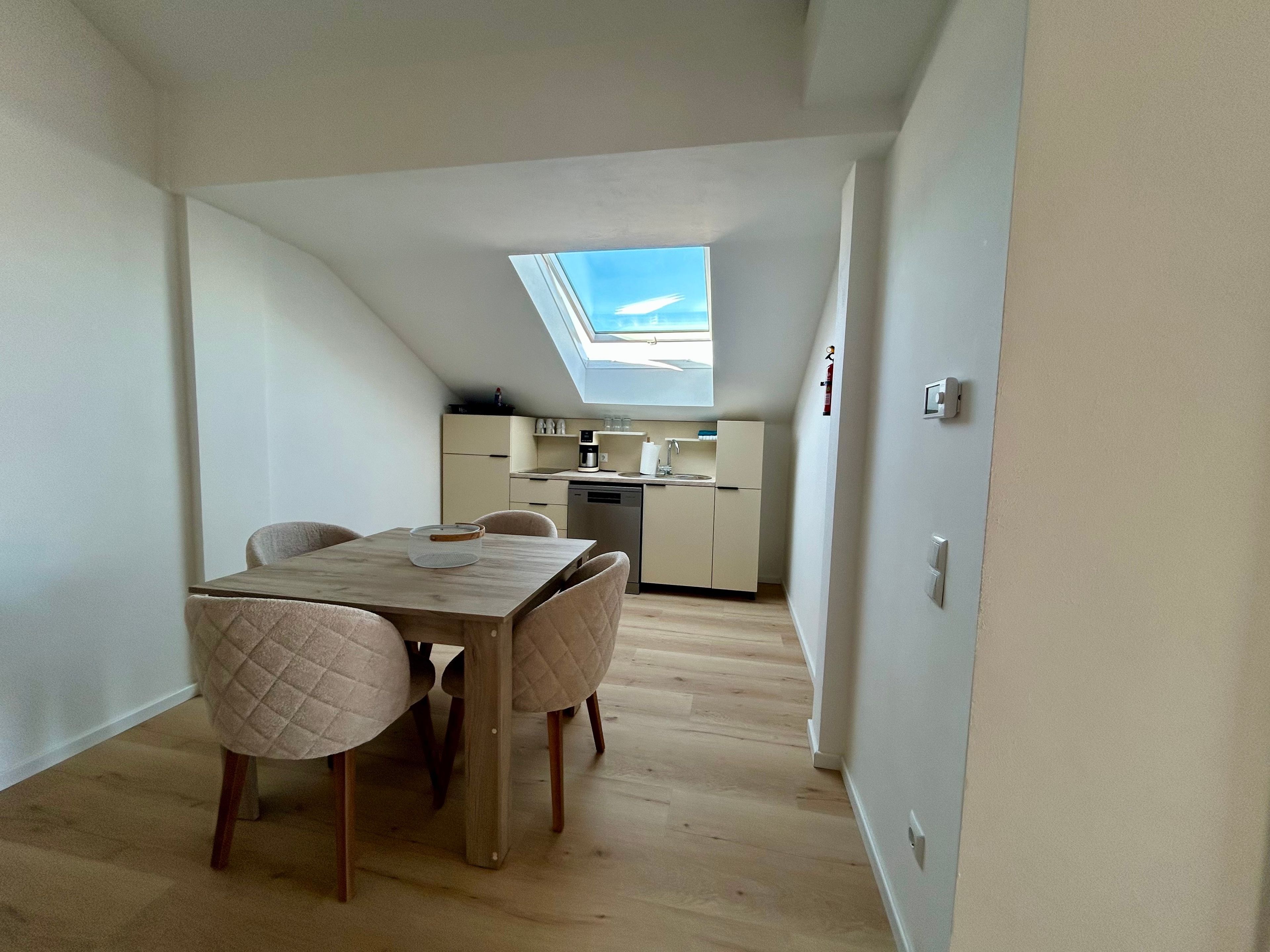 Eine kompakte Küche mit Oberlicht, ein Essbereich mit Tisch und Stühlen und eine sichtbare Decke.
