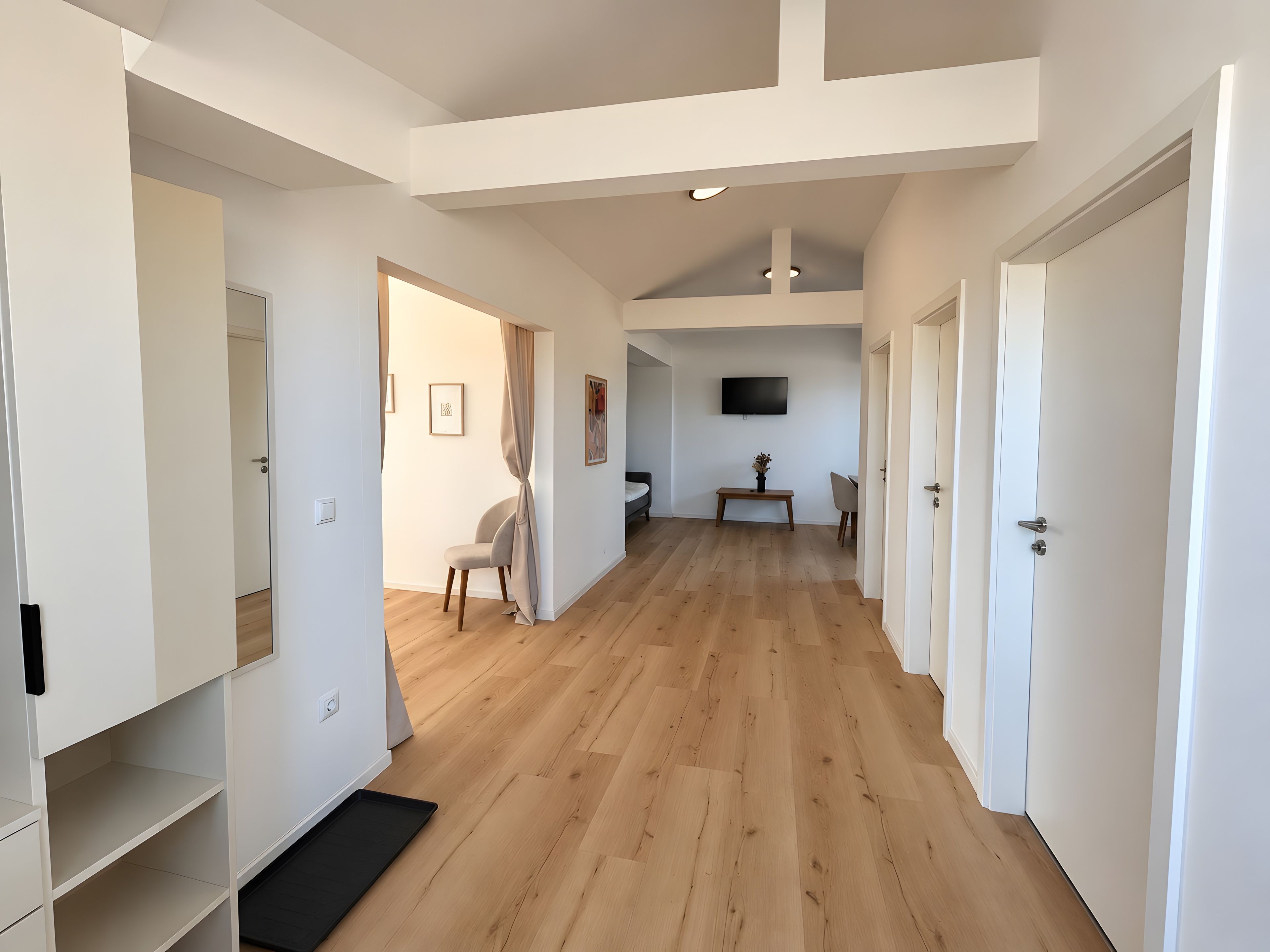 Un hall d’entrée spacieux, doté d’un plancher en bois, de murs blancs et d’un plafond avec des poutres apparentes.
