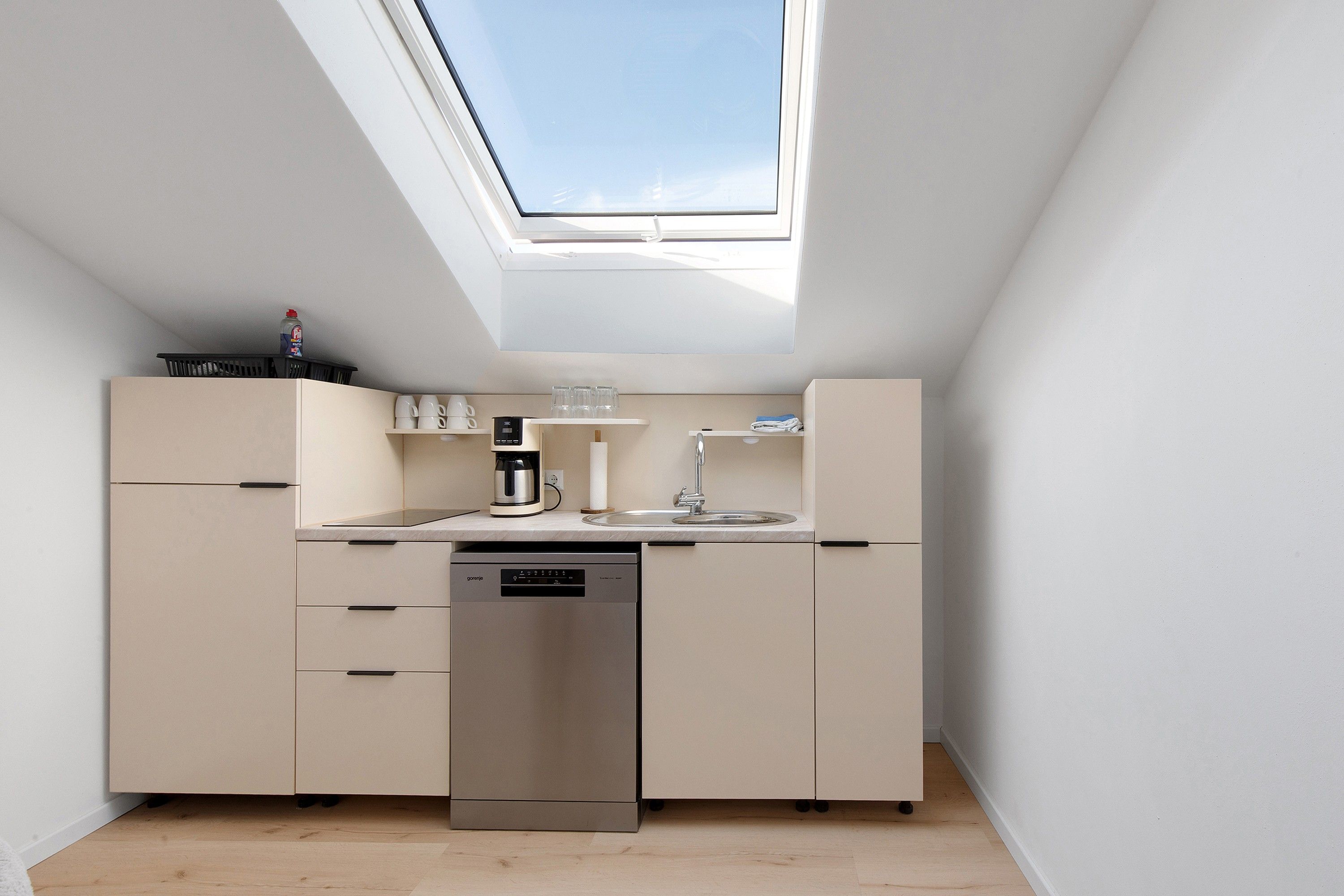 Eine kompakte Küche mit Dachfenster, einer Kaffeemaschine und einem Geschirrspüler.
