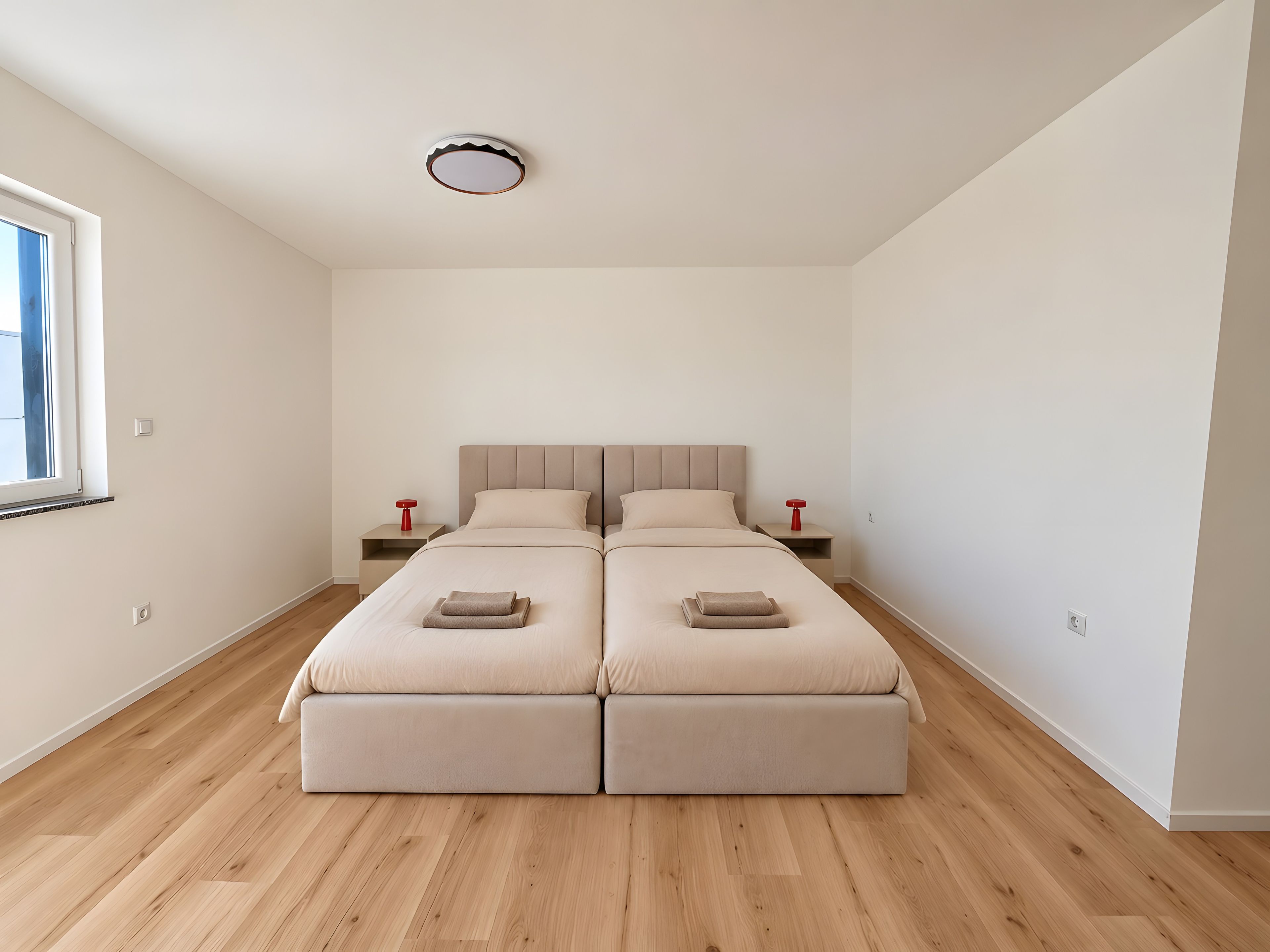 Ein schlicht eingerichtetes Schlafzimmer mit Doppelbett, Nachttischen und einer Deckenleuchte.