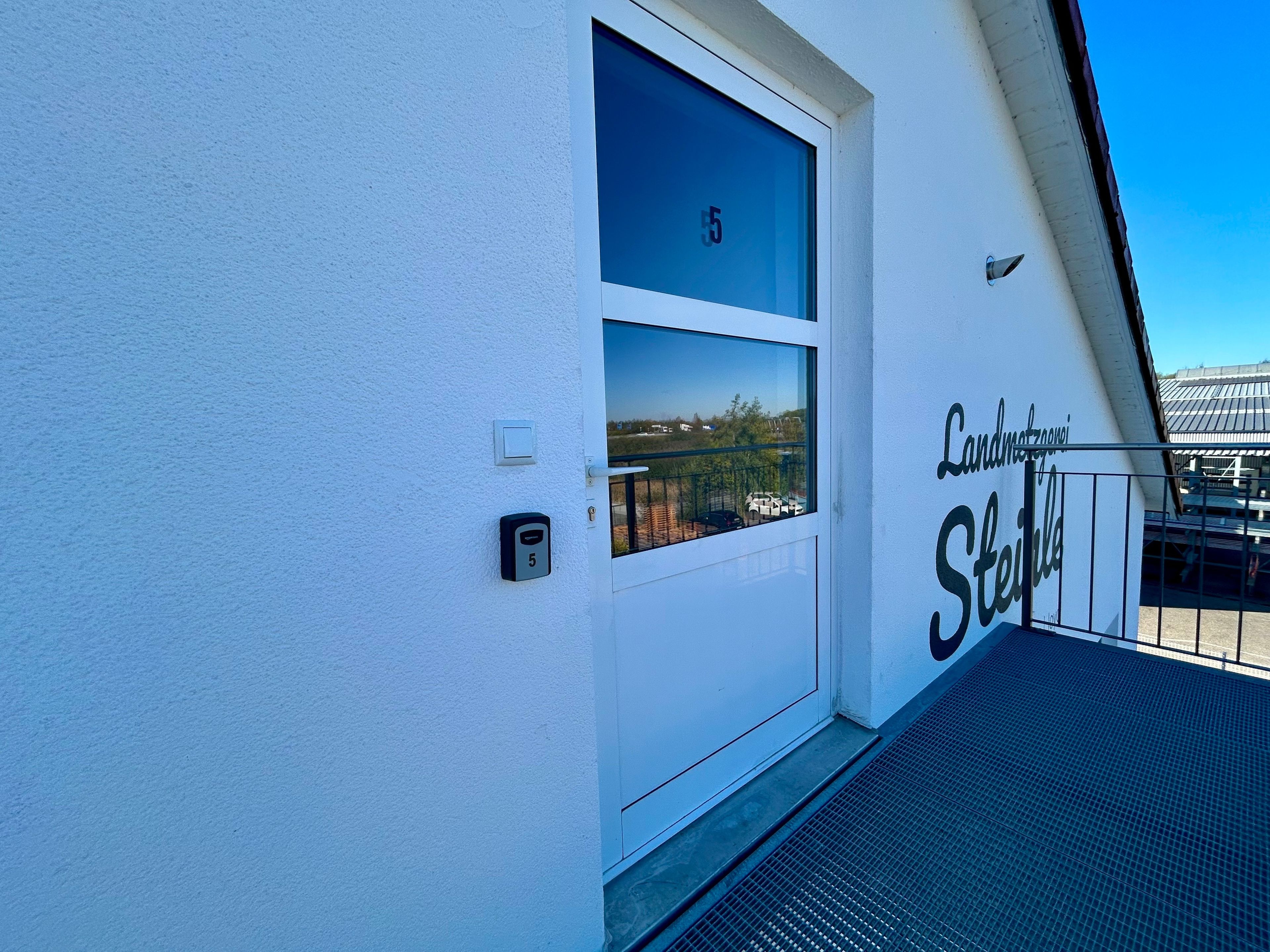 A white building with a window and a door, a number 5 sign, and the text 'Landhaus Steuble' on the side.