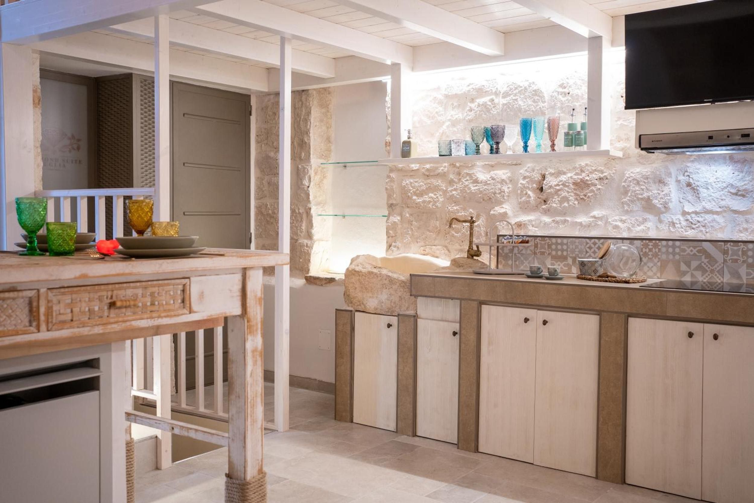 A kitchen with a stone backsplash, a built-in sink, and a flat-screen TV mounted above the counter.