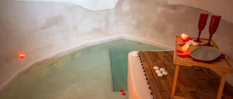 Un cuarto de spa con una piscina pequeña, una terraza de madera y una mesa con velas y un cuenco.