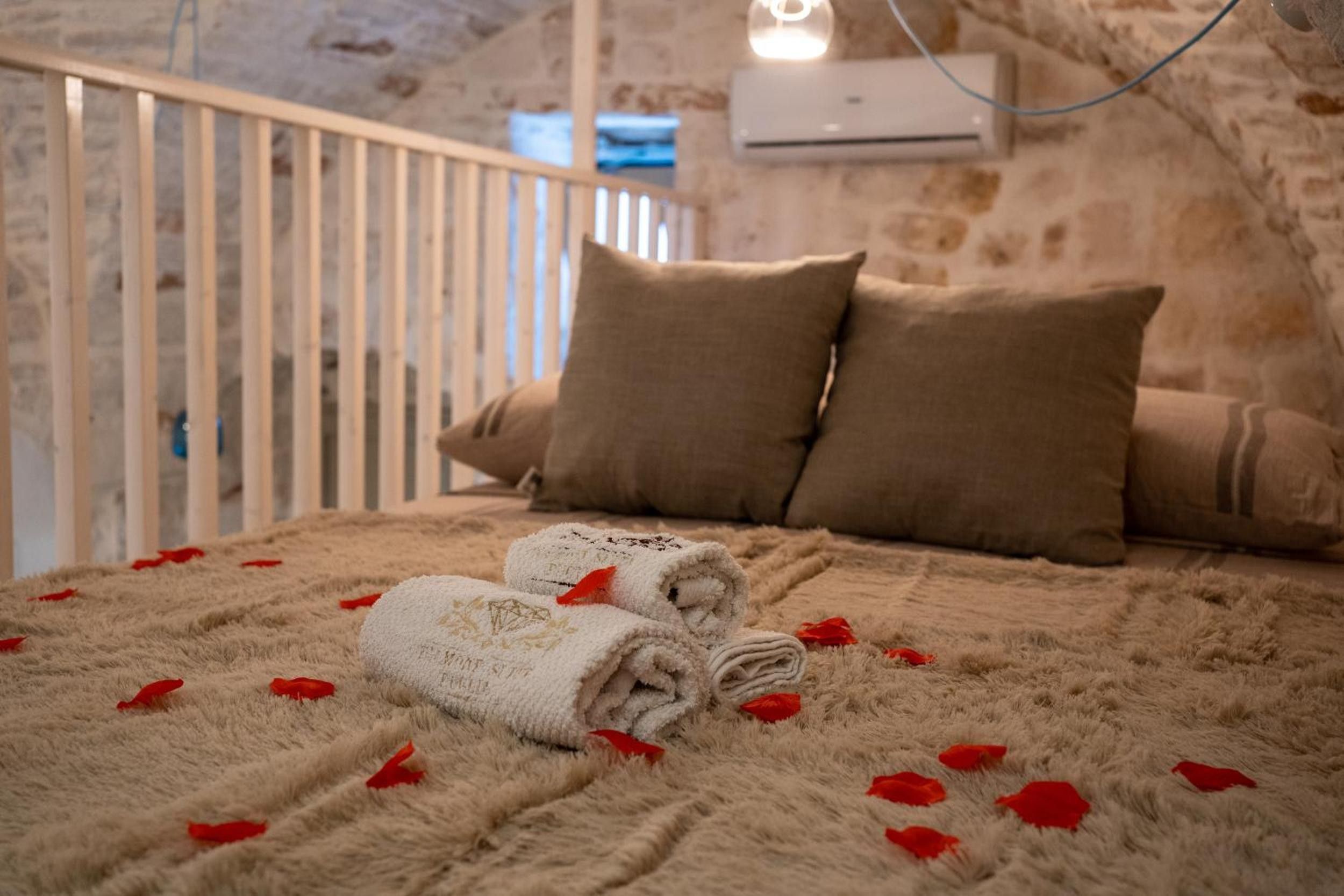 A bed with rolled towels and scattered rose petals, a white railing, and a wall-mounted air conditioning unit.