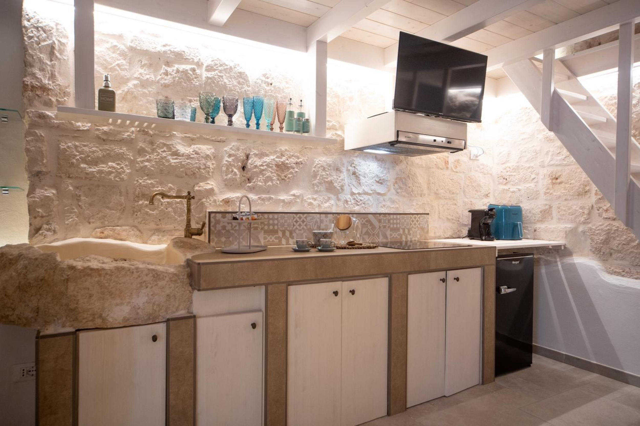 A kitchen with a stone wall backsplash, a built-in oven, and a flat-screen TV mounted above the counter.
