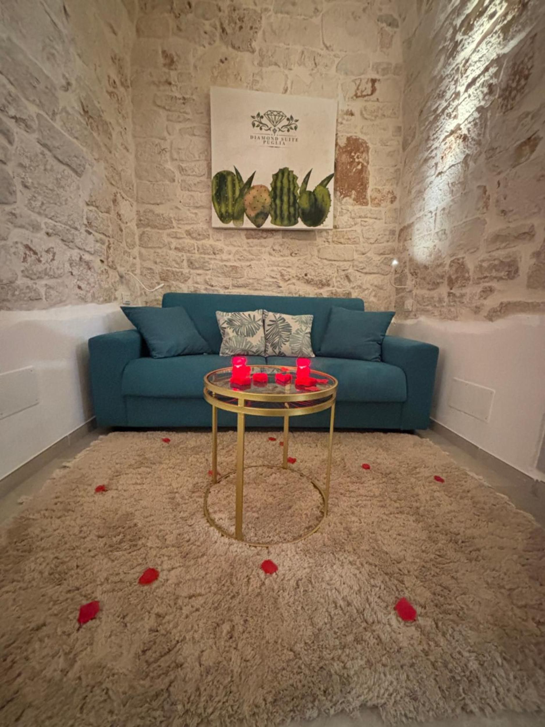 A room with a stone wall, a blue sofa, a glass coffee table with red objects, and a carpet with red petals.