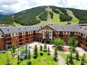 A large, multi-story hotel with a central courtyard, surrounded by lush greenery and a mountain backdrop. - Copper Springs Getaway with Great Ski Access (Copper Mountain)