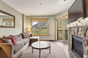 A living room with a sofa, a coffee table, a fireplace, and a large window with a mountain view. - Copper Springs Getaway with Great Ski Access (Copper Mountain)