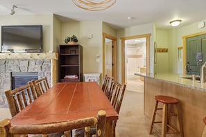 A dining area with a wooden table and chairs, a television mounted above, and a kitchen area with a bar stool. - Copper Springs Getaway with Great Ski Access (Copper Mountain)