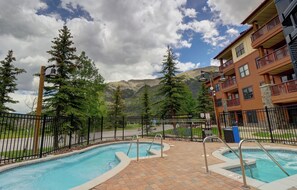 A pool area with a view of mountains, a fenced deck, and a building with balconies. - Copper Springs Getaway with Great Ski Access (Copper Mountain)
