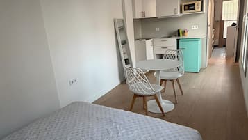 Een slaapkamer met een bed, een stoel, een bureau en een kitchenette op de achtergrond.