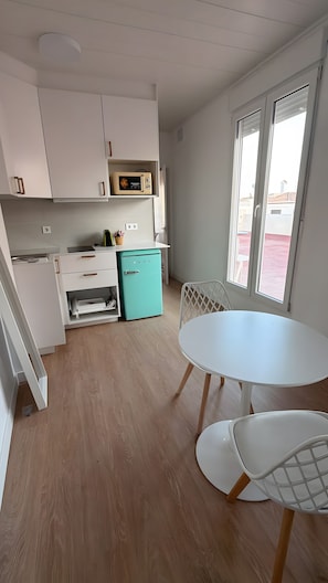 Una cuina moderna amb armaris blancs, un mini-frigorífic color turquesa i una zona de menjador amb taula i cadires blanques.