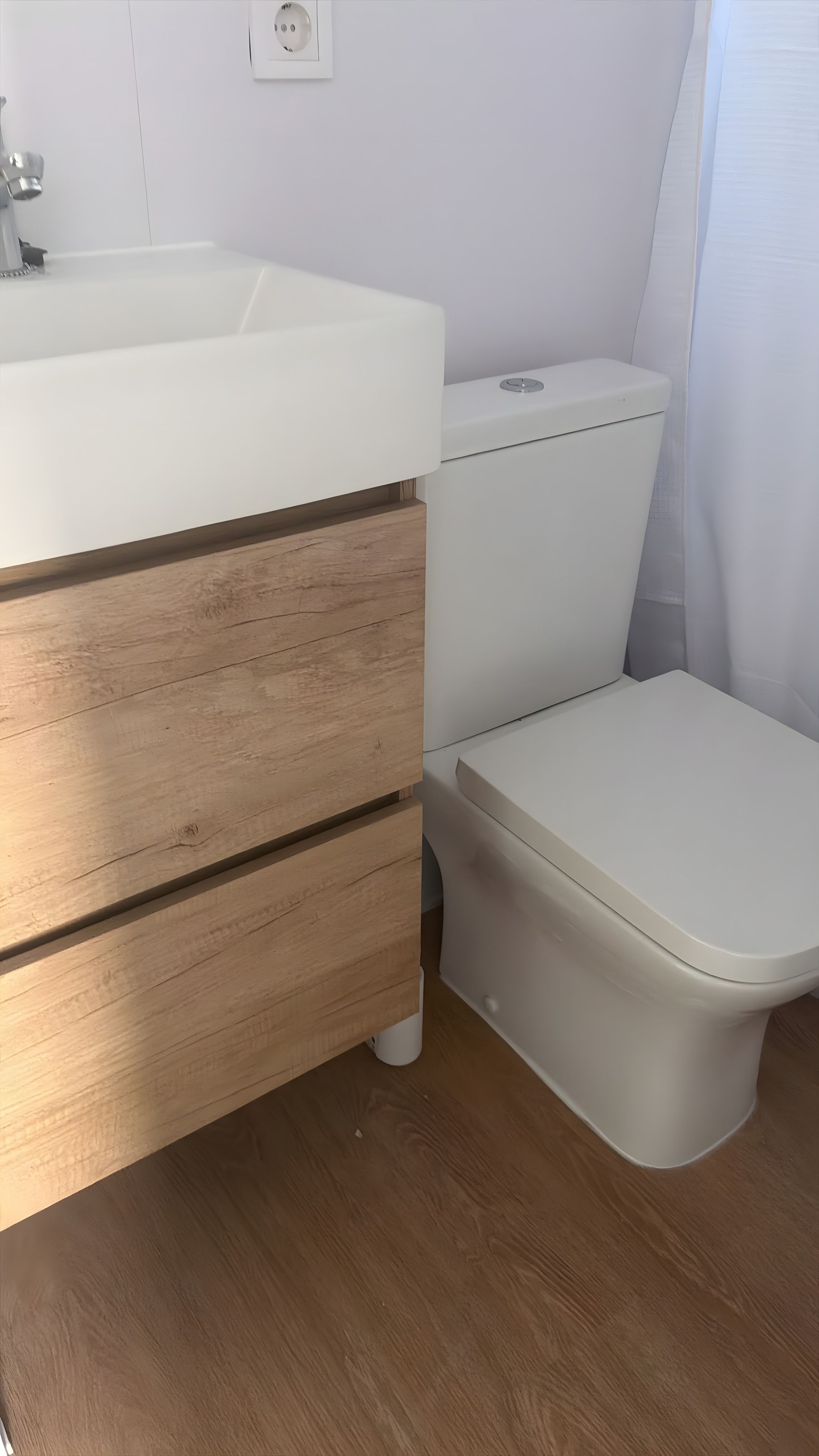 Een badkamer met een wit wastafelmeubel, houten lades, een toilet en een witte douchegordijn.