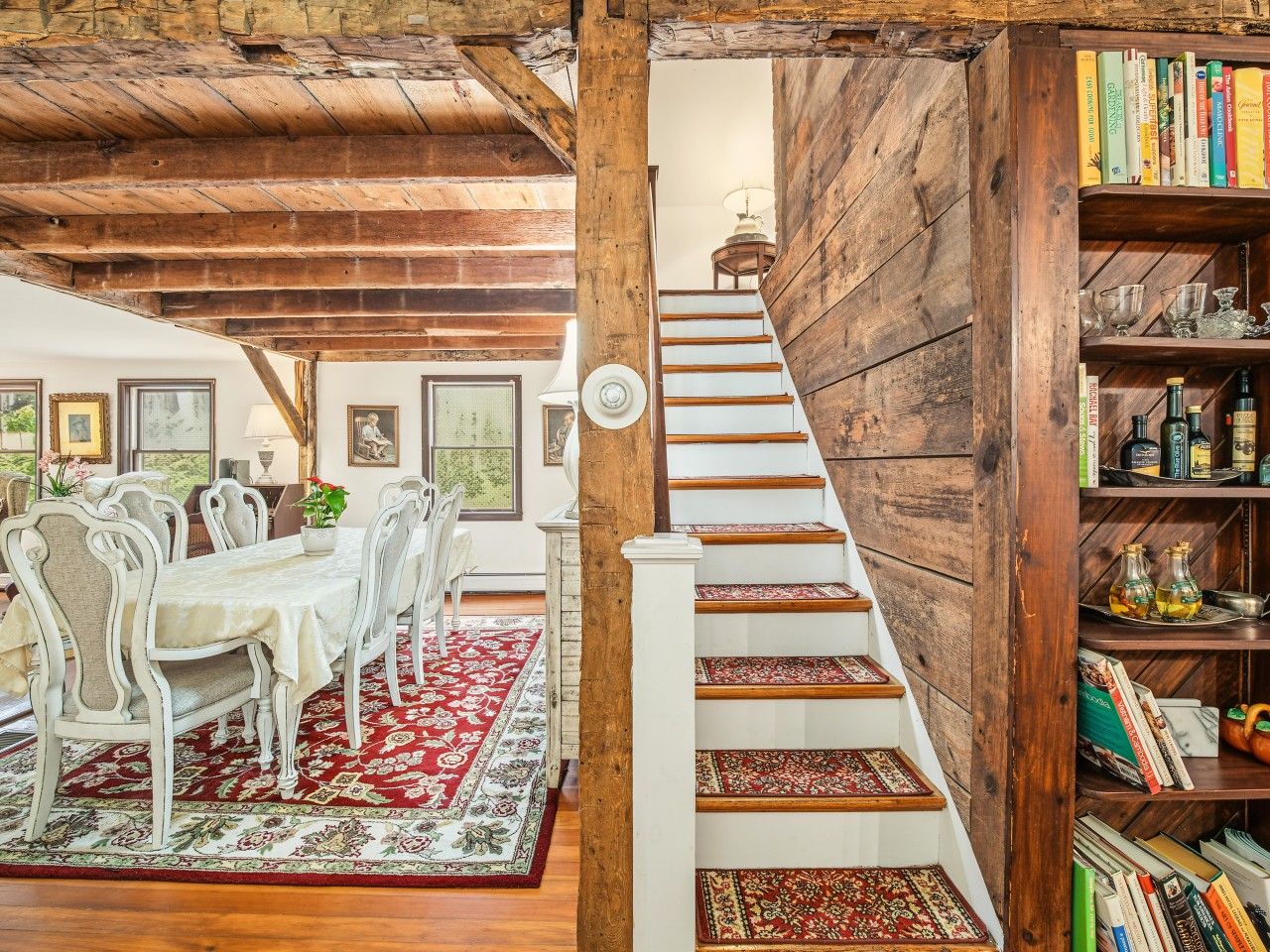 A dining area with a table and chairs, a staircase with a wooden railing, and a bookshelf with books and decorative items.