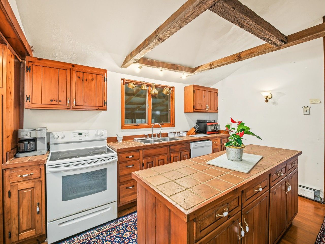 A kitchen with wooden cabinets, a stove, a sink, and a window with pots hanging above.