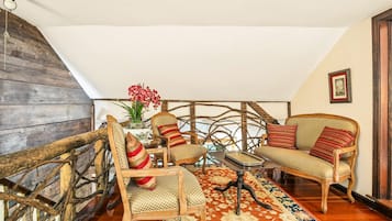 Een loft-achtige kamer met een houten trap, rieten meubels en een kamerbreed tapijt met een patroon.