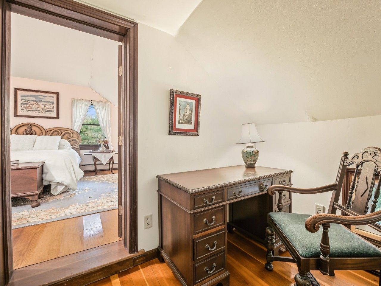 A room with a wooden desk, a chair, a bed, and a view of an outdoor area.