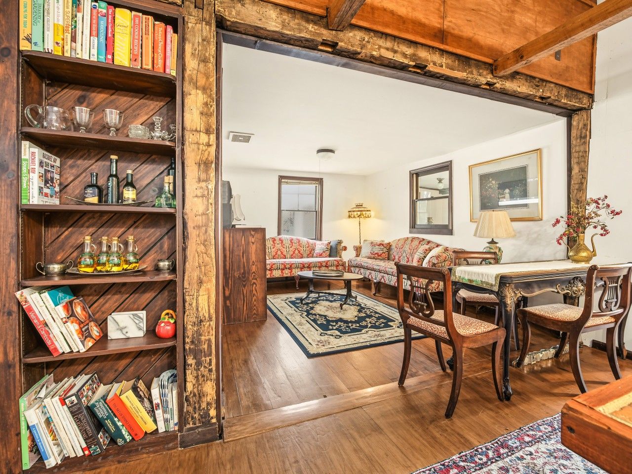 Un accogliente soggiorno con una libreria in legno, un divano, un tavolo da pranzo con sedie e un tappeto decorato.