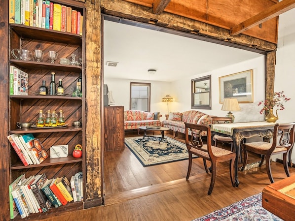 Una sala de estar acogedora con una estantería de madera, un conjunto de sofás, una mesa de comedor con sillas y una alfombra estampada.