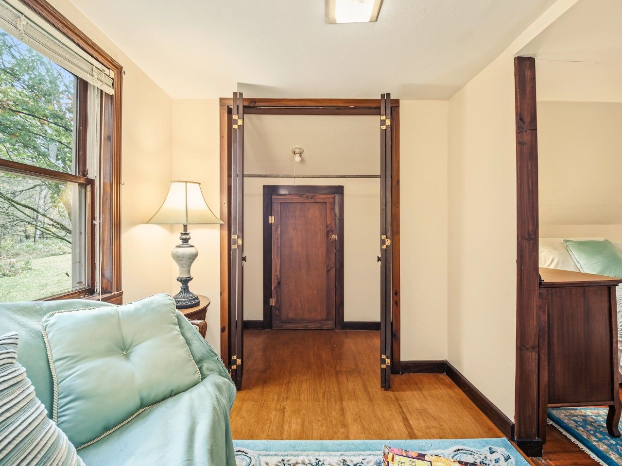 A room with a bed, a lamp, a window, and a door leading to another room.