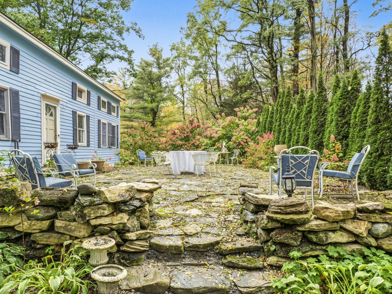 Eine Steinterrasse mit Gartenmöbeln, umgeben von einem Garten mit verschiedenen Pflanzen und Bäumen.
