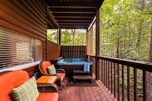 A wooden deck with a hot tub, wicker furniture, and a view of a forest. - Hot Tub-Fireplace-Private-Honeymoon-Hiking-Relax (Sevierville)