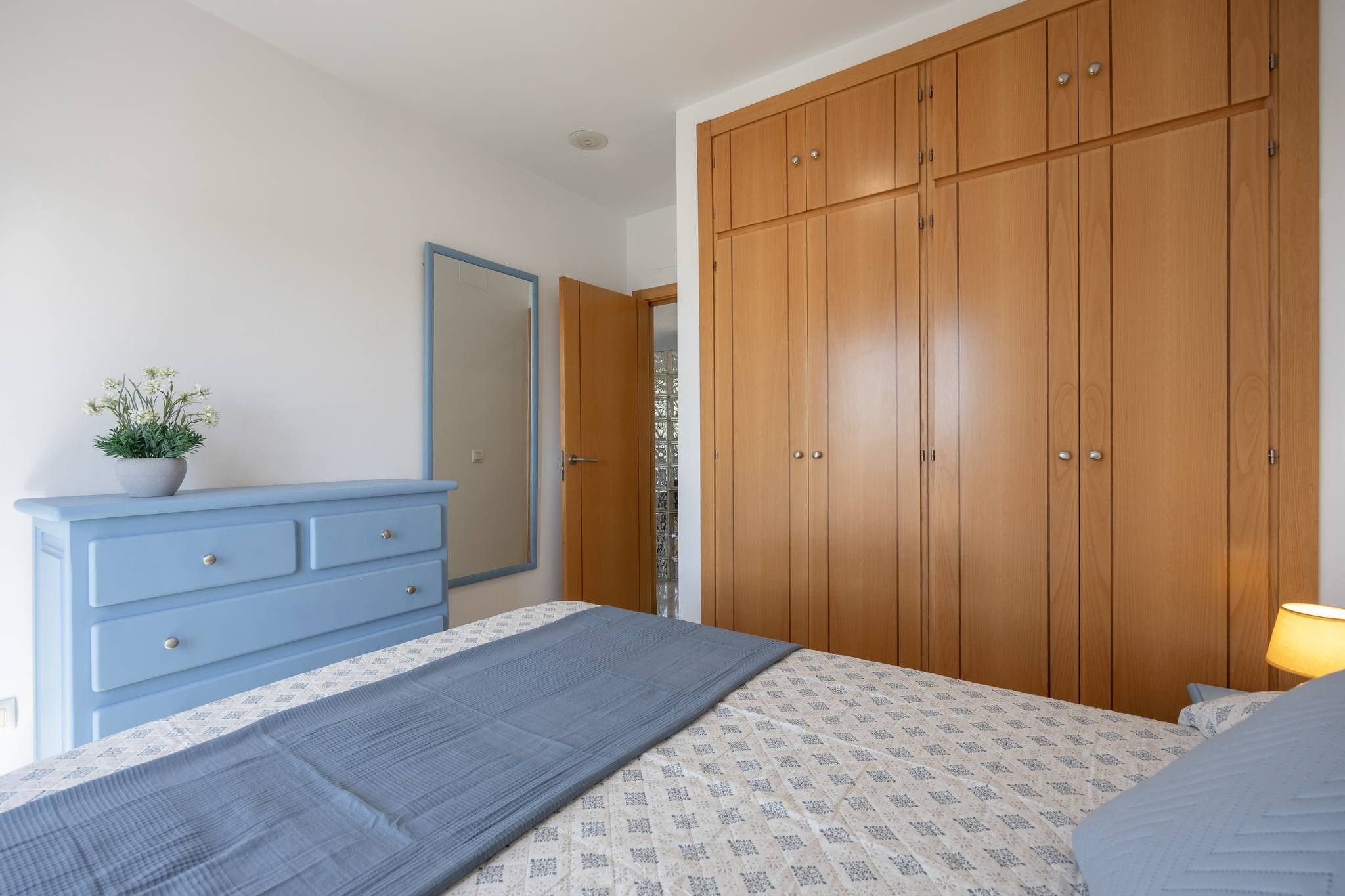 A bedroom with a bed, a dresser, a wardrobe, and a potted plant.