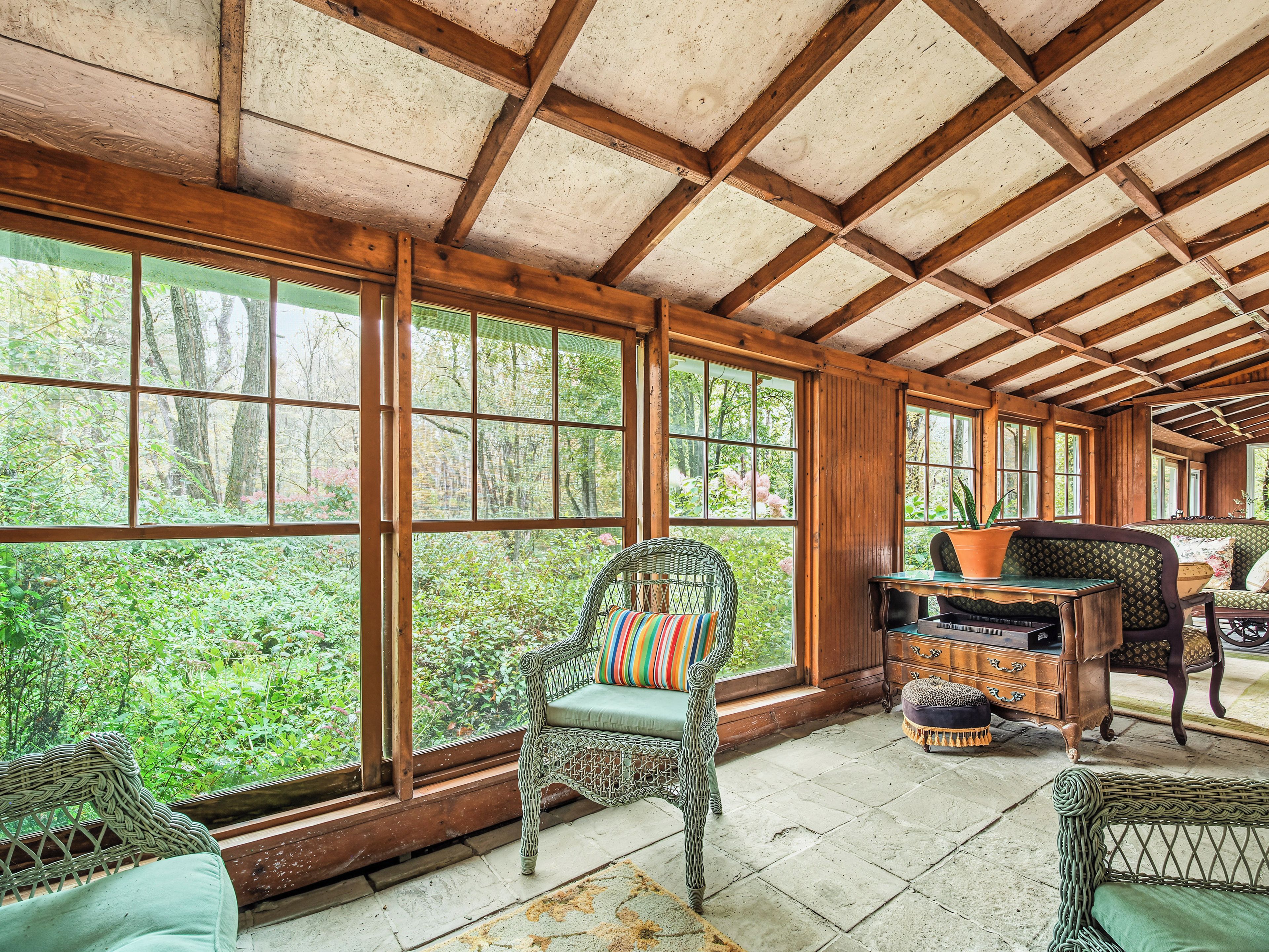 Ein Zimmer mit großen Fenstern, Korbmöbeln und einer Holzbalkendecke.
