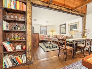 A cozy living room with a wooden bookshelf, a patterned sofa, and a dining table with chairs.