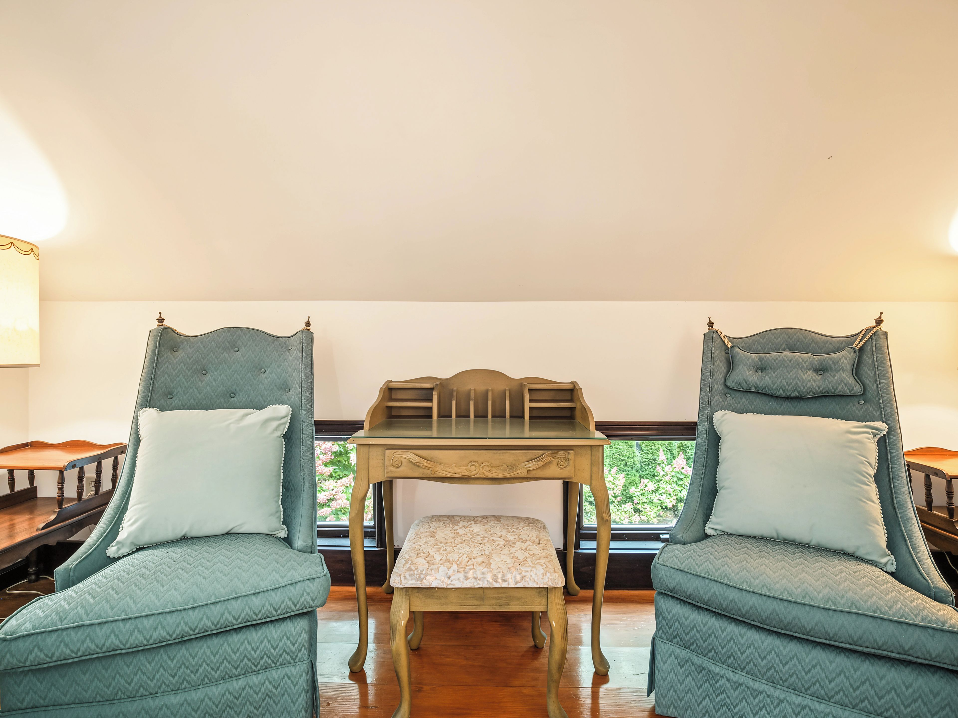 A room with two upholstered chairs with wooden frames, a small wooden table, and a view through a window.