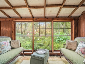 A room with a large window, wooden beams, two upholstered sofas with floral cushions, and a small table.