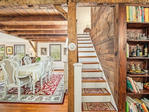 A dining area with a wooden staircase leading to a bookshelf filled with books and bottles.