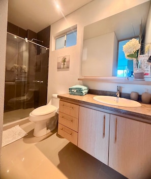 A modern bathroom with a glass shower enclosure, a white toilet, a vanity with a sink, and a mirror above the mirror. - Reserva del Mar (Santa Marta)