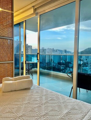 A modern hotel room with a large bed, a massage chair, and a balcony with a city view. - Reserva del Mar (Santa Marta)