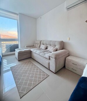 A modern living room with a sectional sofa, a patterned rug, and a view through a large window. - Reserva del Mar (Santa Marta)