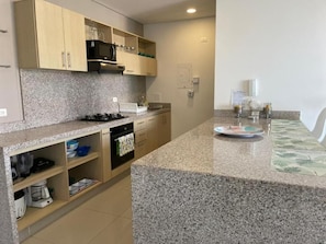 A modern kitchen with granite countertops, wooden cabinets, and a built-in microwave. - Reserva del Mar (Santa Marta)