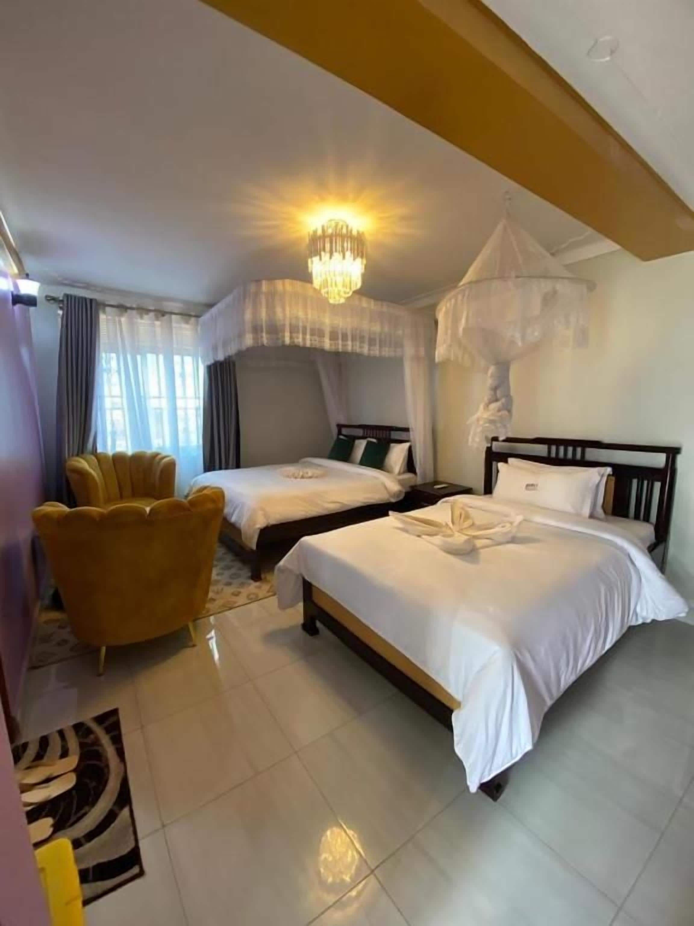 Une chambre d’hôtel avec deux lits, un lustre, un lit à baldaquin et un fauteuil jaune.