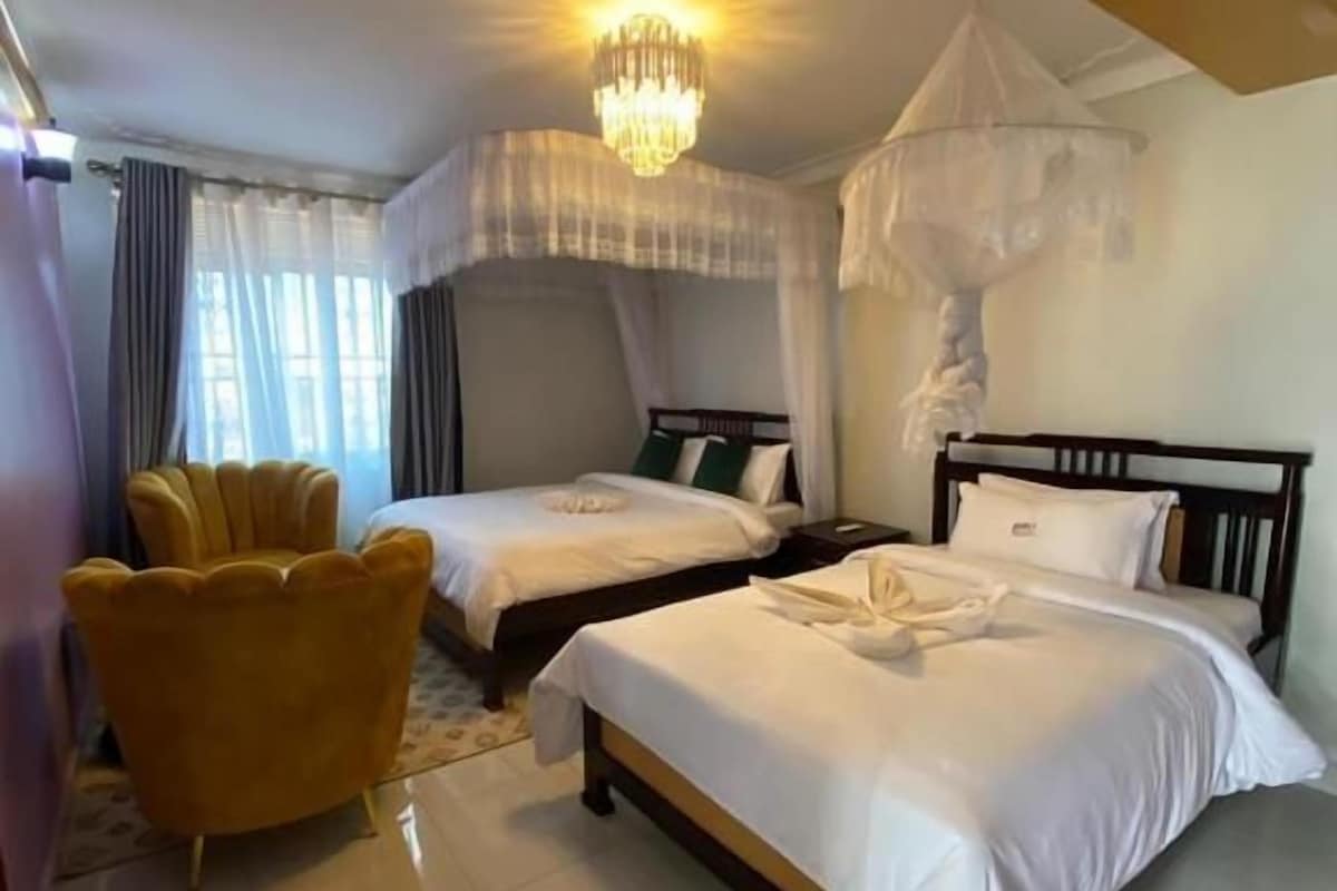 Habitación de hotel con dos camas, un candelabro, una cama con dosel y un sillón amarillo.