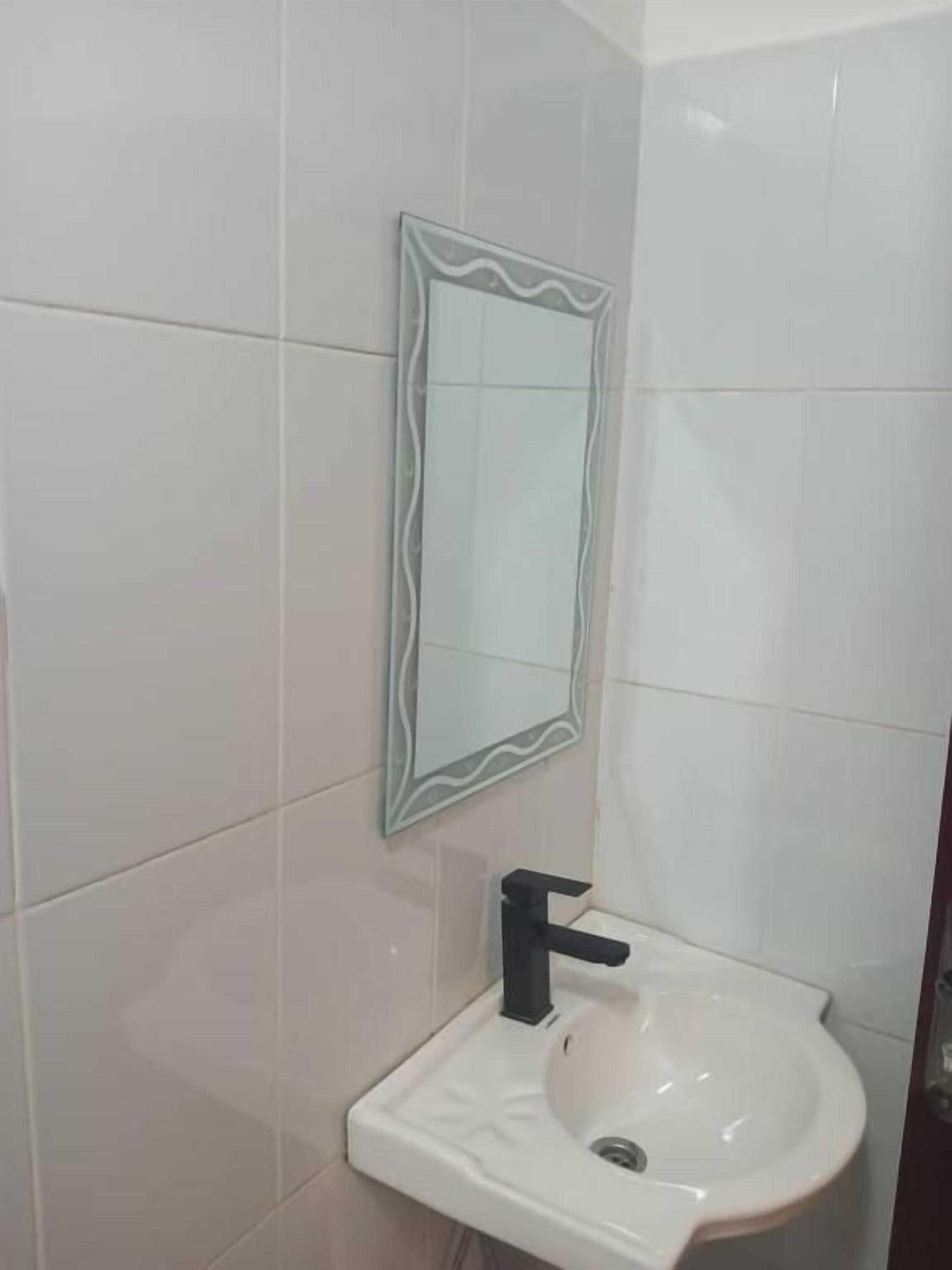 Un baño con lavamanos blanco, grifo negro y espejo con marco ondulado.