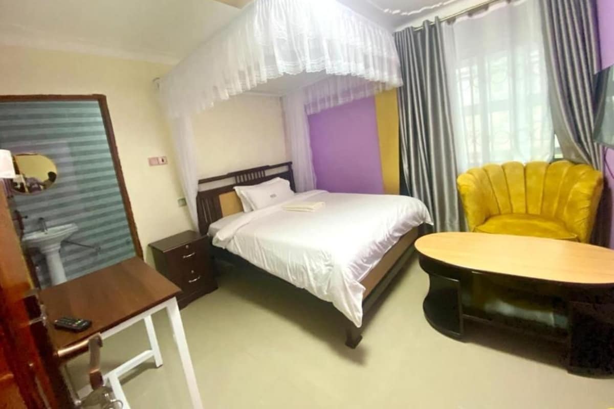 Una habitación de hotel con cama, mesita de noche, silla y una pequeña mesa con otra silla.