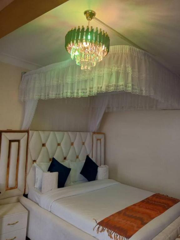 Une chambre à coucher avec une tête de lit capitonnée, un lit recouvert de linge de lit blanc, une table de chevet en bois et un lustre vert.