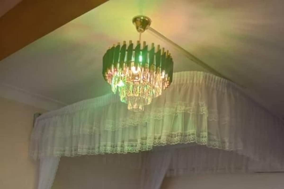 Un dormitorio con cabecera capitonada, cama con ropa de cama blanca, mesita de noche de madera y una lámpara de araña verde.