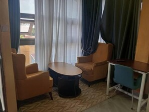 Una habitación con dos sillones de cuero, una mesita, un escritorio con silla y vistas a través de una ventana con cortinas.