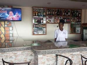 Zona de bar con mostrador, sillas y televisor mostrando un video musical.